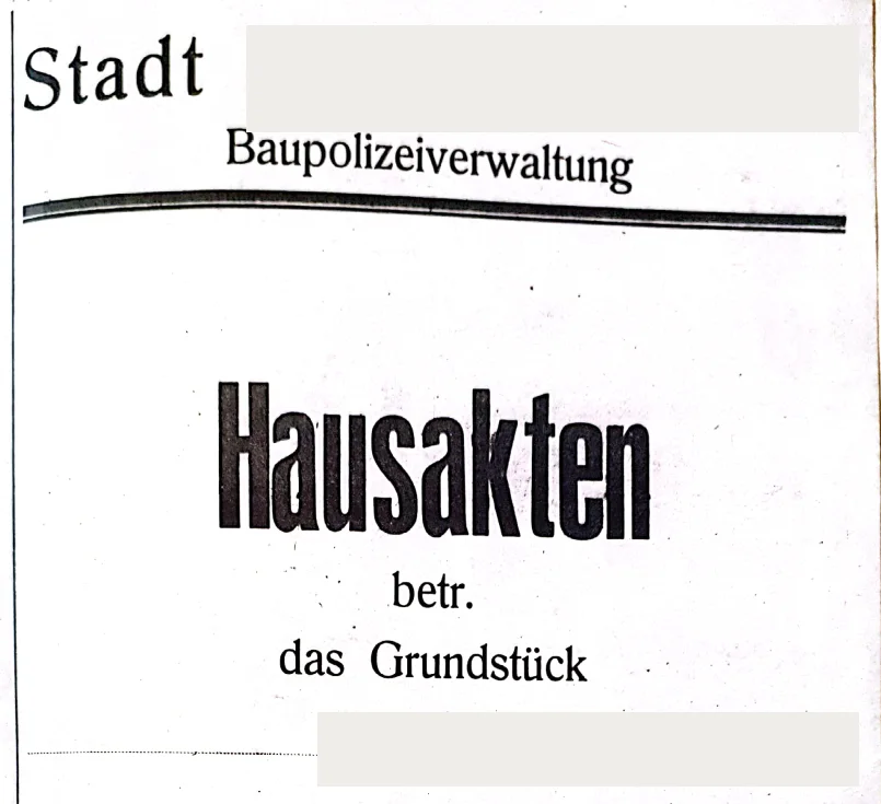 Titelblatt einer historischen Hausakte der Baupolizeiverwaltung mit der Aufschrift Hausakten betr. das Grundstück; Stadtname und Straße sind unkenntlich gemacht