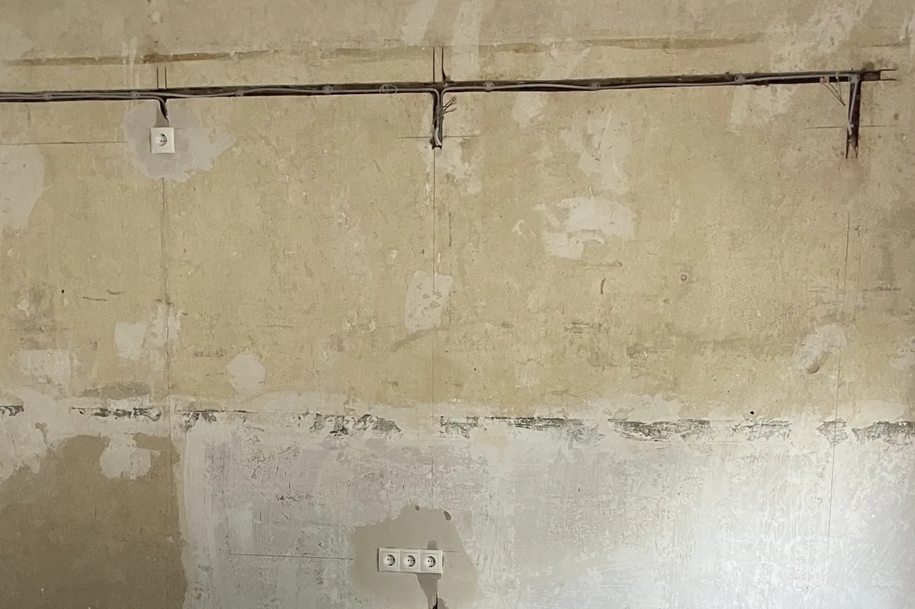 Altbauwand ohne Putz mit einem Elektrokabel in einem waagerechten Schlitz im Mauerwerk, einer Steckdose links und einem Dreier-Steckdosenblock unten