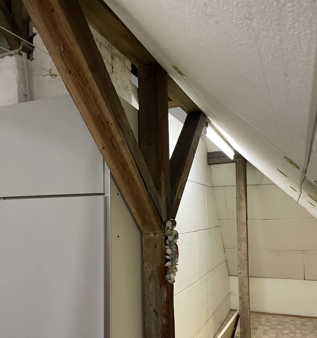 Holzstrebe, Stiel und Pfette in einem ausgebauten Dachraum neben hellen Dämmplatten an der Dachschräge; das Holz zeigt keine Risse und keine abplatzende Oberfläche
