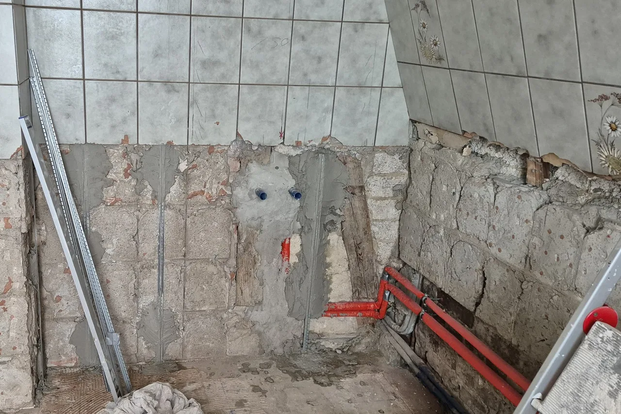 Halb abgeschlagene Badezimmer-Wandfliesen über freigelegtem Mauerwerk mit neu verlegten rot gedämmten Wasserleitungen