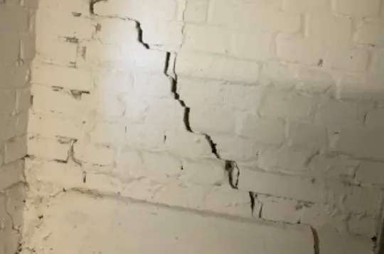 Weiß gestrichene Kellerwand aus Ziegel mit durchgehendem Riss, der in Stufen den Fugen folgt