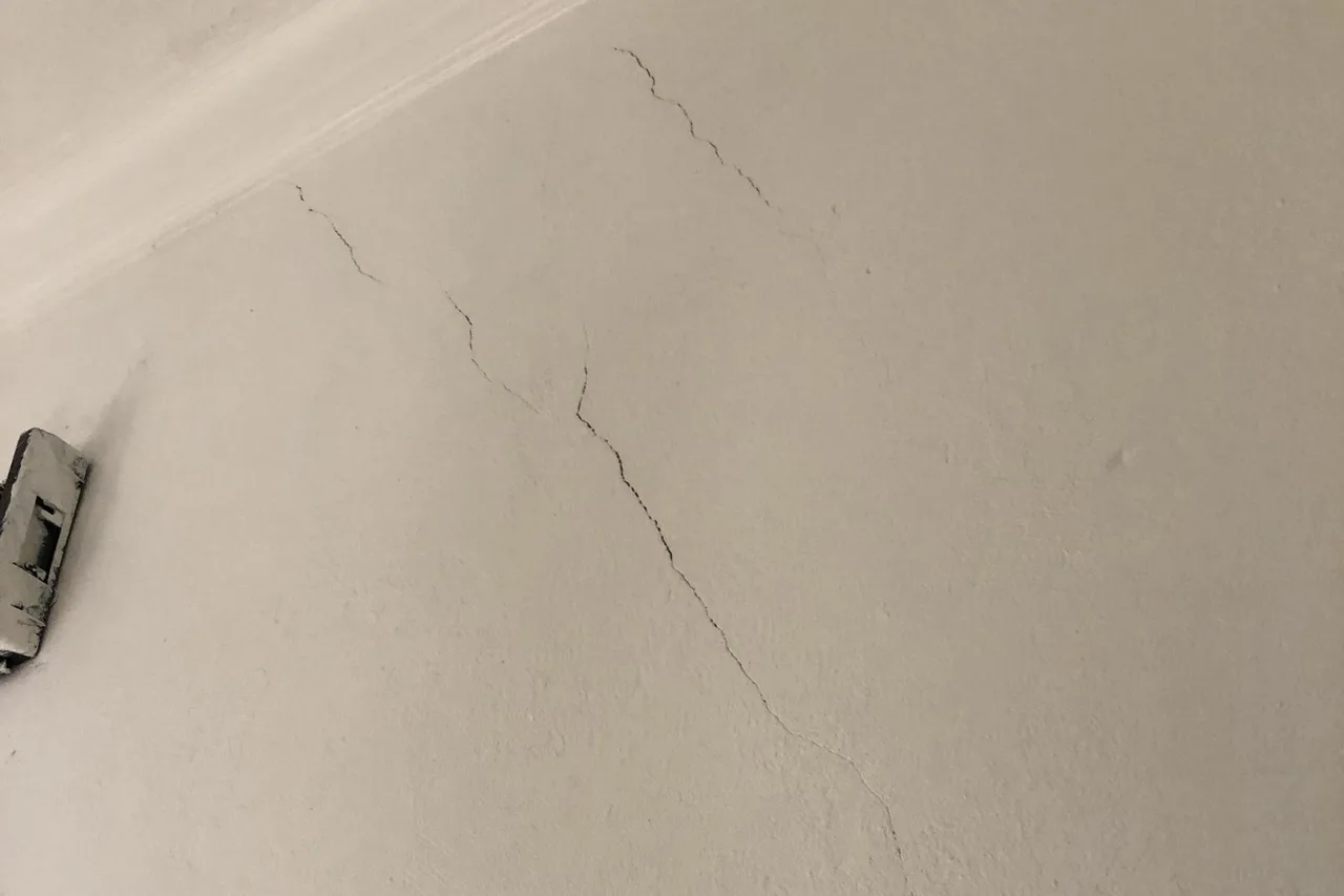 Weiß verputzte Wand unter der Decke mit mehreren feinen, in Absätzen verlaufenden Rissen im Putz