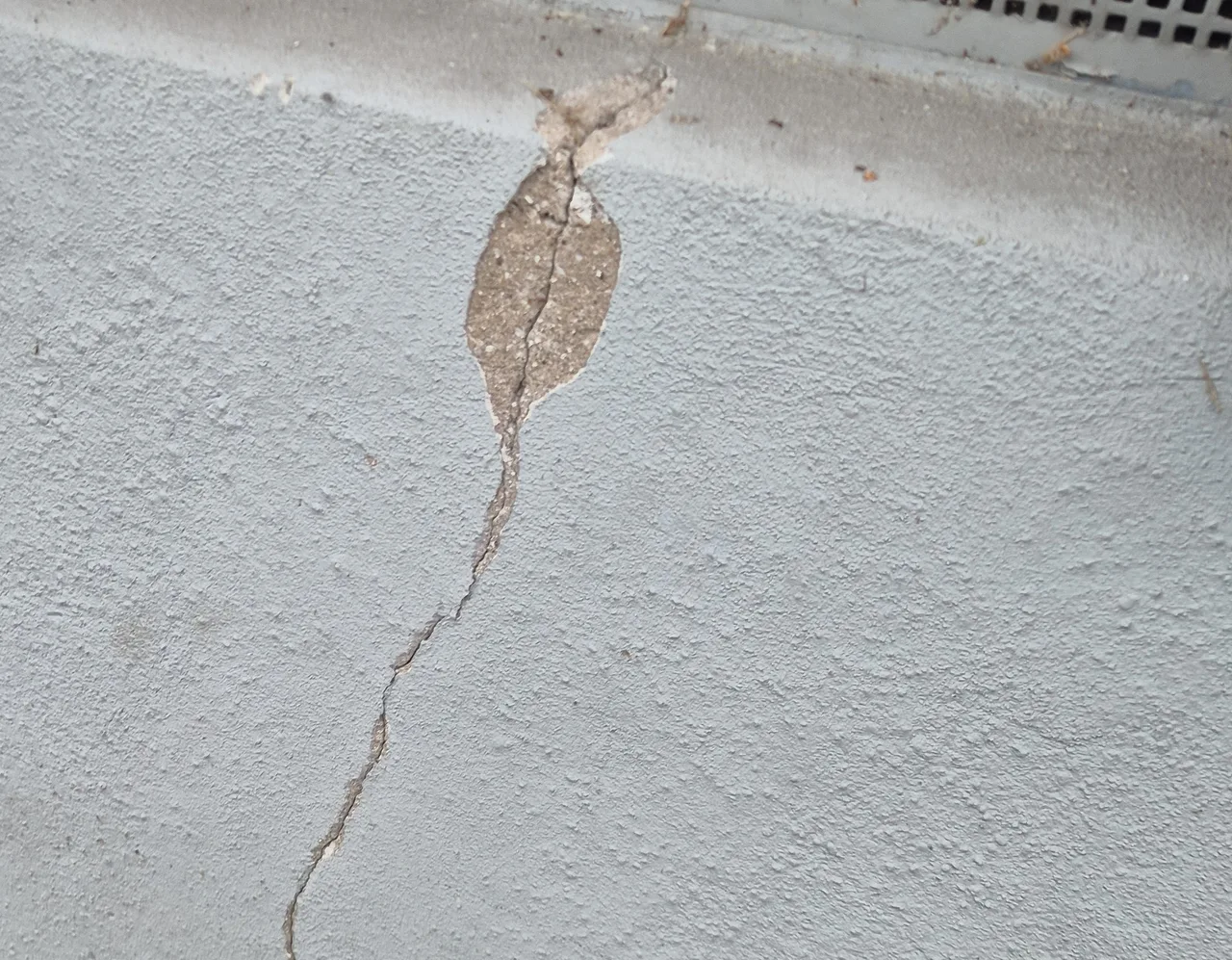 Grau verputzter Sockel mit einem senkrechten Riss, der oben in einer ausgebrochenen Putzstelle beginnt