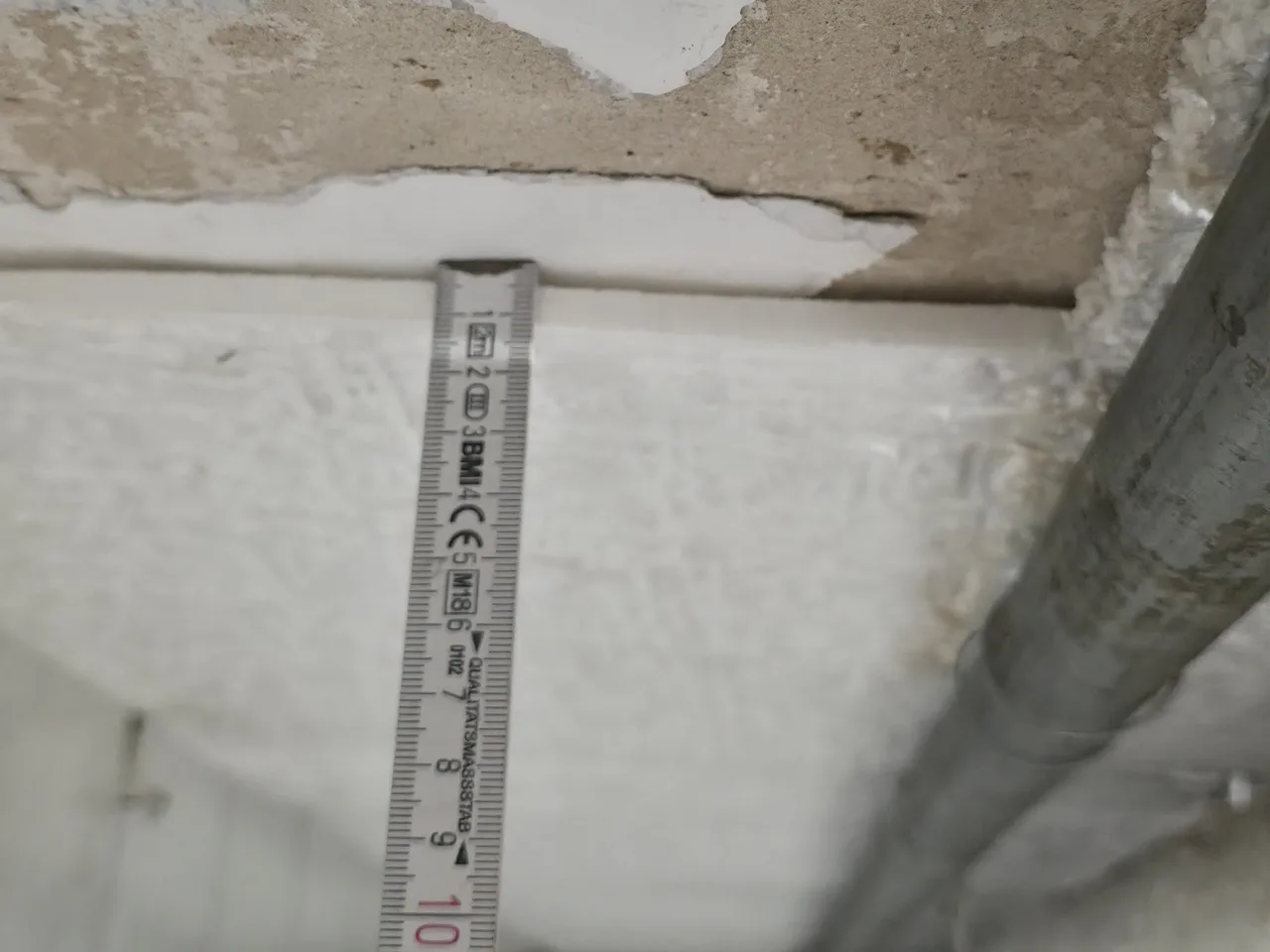 Eigenes Foto: Kante einer Dämmplatte an einer Kellerdecke mit abgeplatztem Putz und angelegtem Zollstock