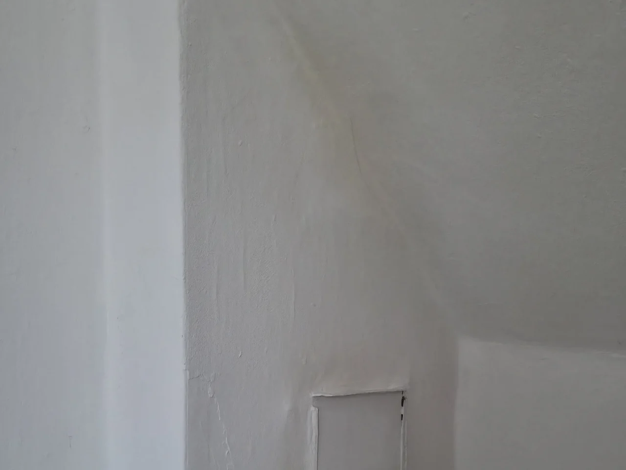Weiß gestrichene Dachschräge im Dachgeschoss mit gelblichem Streifen entlang der Schrägenkante und einer Reinigungsluke im Putz darunter